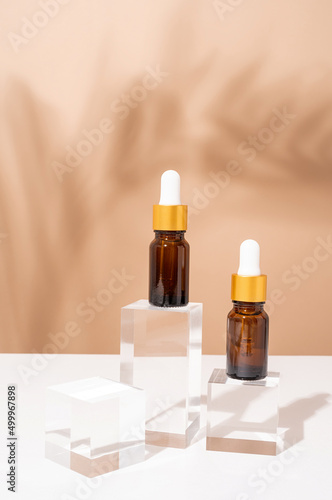 Amber glass dropper bottles with a pippette with white rubber tip on glass podium and beige background, mockup design