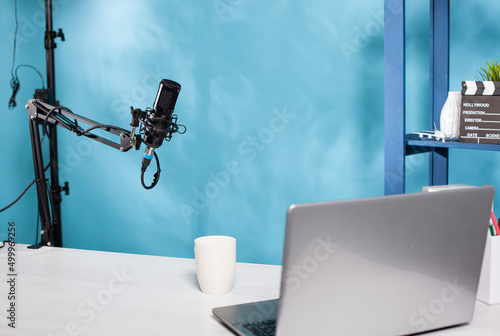 Professional microphone swivel boom arm stand in empty vlog broadcasting studio used for recording social media content. Audio live broadcast desk setup with digital mic and laptop computer. photo