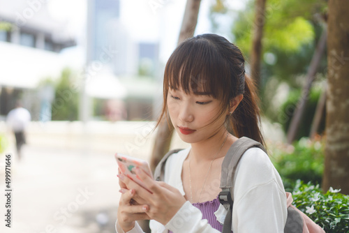 Young adult asian female student using digital mobile phone for online message at outdoor