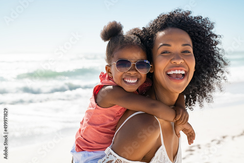 Fotografia Happy young mother giving laughing daughter piggyback ride at beach