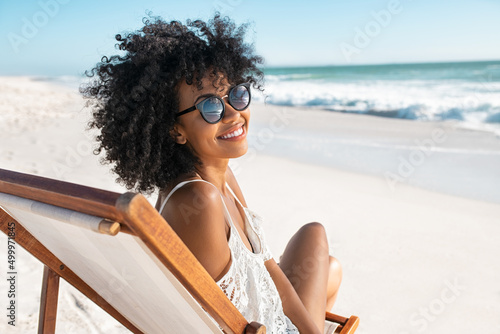 Stampa su tela Happy smiling african woman sitting on deck chair at beach