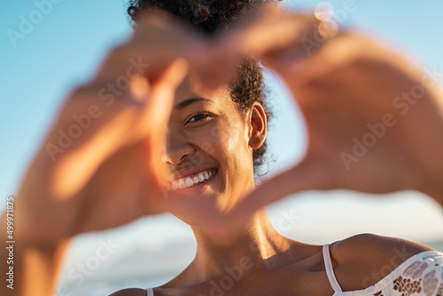 Картината върху платно Black lovely woman making hand heart at beach during sunset