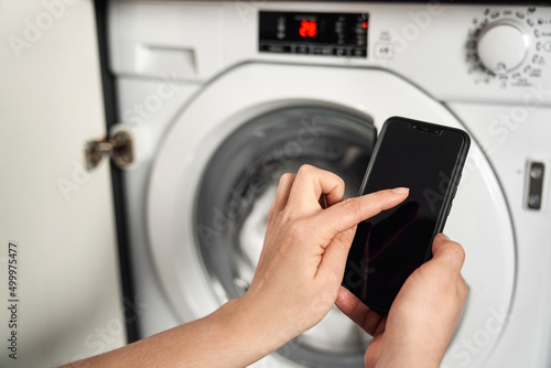 Close up of woman holding mobile phone and turn on washing machine