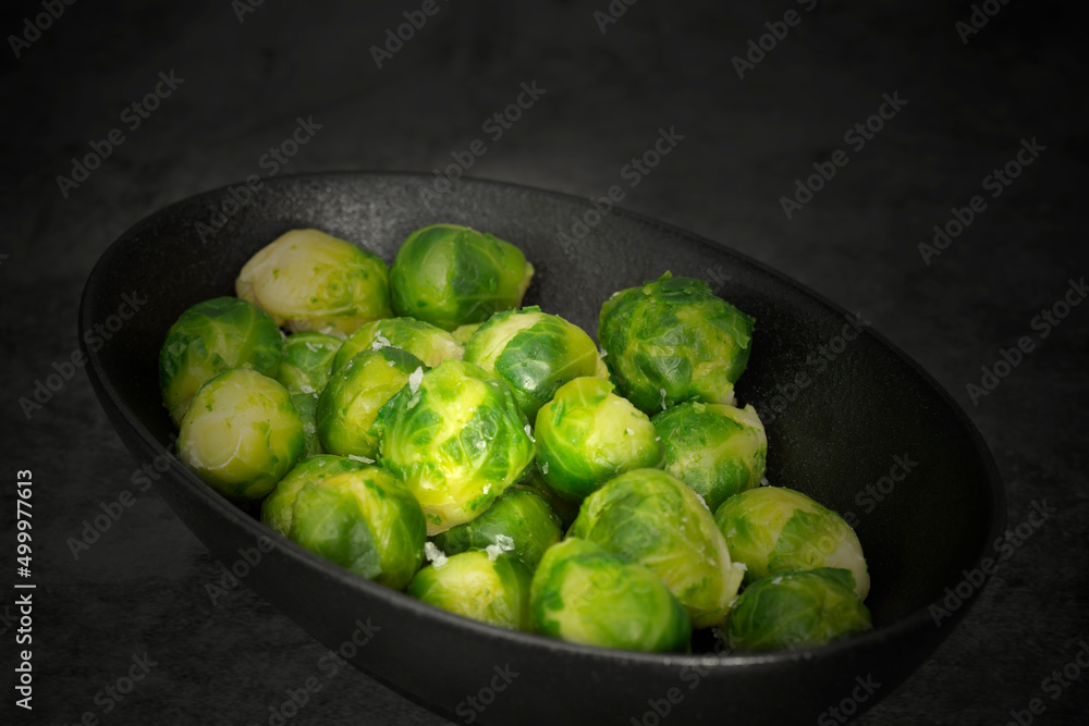 Brussels sprouts seasoned with sea salt in a black dish. On a stone background Brussels sprouts seasoned with sea salt in a black dish. On a stone background