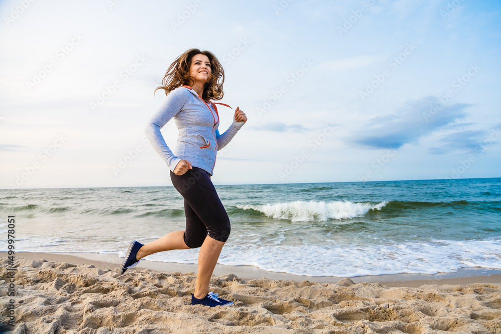 Young woman running, jumping on beach
