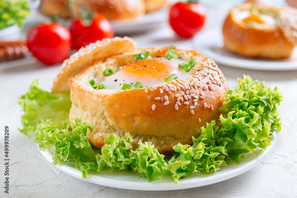 Breakfast eggs. Baked buns stuffed with eggs and bacon and fresh herbs on plates on a light background. Close up Breakfast eggs. Baked buns stuffed with eggs and bacon and fresh herbs on plates on a light background. Close up