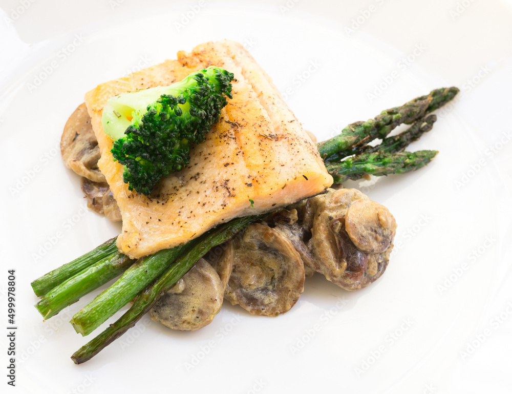 dish of fried river trout fillet with garnish of broccoli, asparagus sprouts and mushroom sauce on white background dish of fried river trout fillet with garnish of broccoli, asparagus sprouts and mushroom sauce on white background