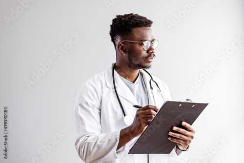 Portrait of smiling black male doctor with stethoscope on white background. Young happy black medical doctor holding medical chart over white studio background, copy space..