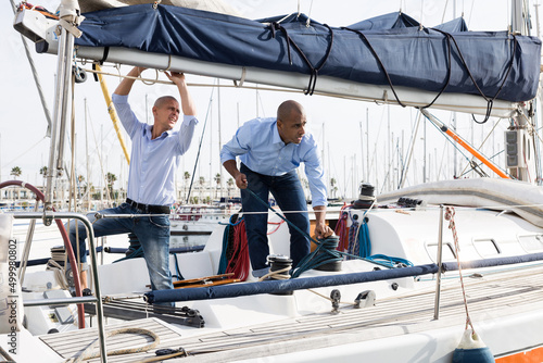 Two young men in blue shirts tidy up private sailing yacht in the seaport