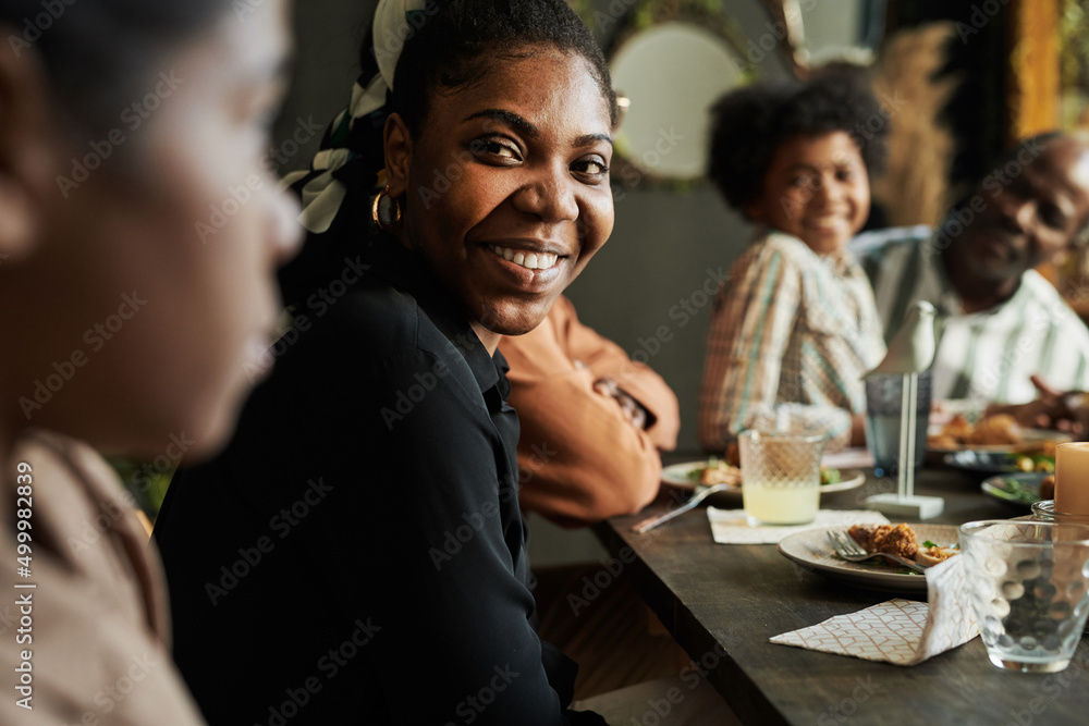 African happy woman talking to her family while sitting at dining table during dinner