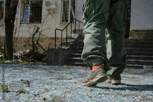 A man in green pants walks on broken glass. Pieces of broken glass lie on the sidewalk after the explosion.