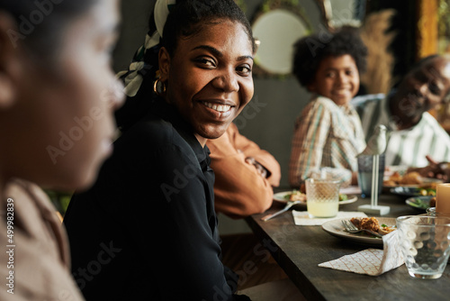 African happy woman talking to her family while sitting at dining table during dinner