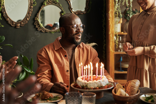 Happy African man in eyeglasses celebrating birthday with his family with birthday cake with candles
