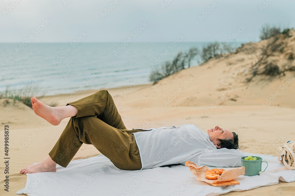 adult woman in the spring at a picnic on the beach by the sea lies on plaid with a smile, enjoyment