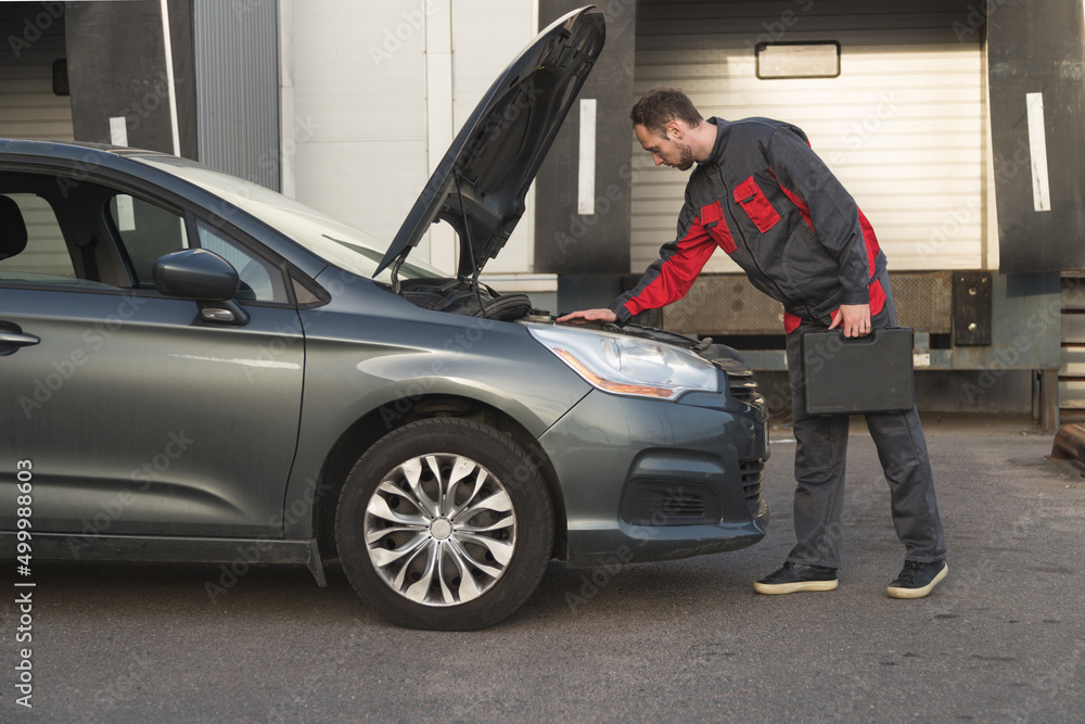 auto mechanic holding case with tools look at car under the hood during vehicle technical inspection auto mechanic holding case with tools look at car under the hood during vehicle technical inspection
