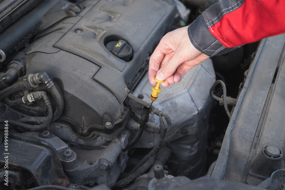 Serviceman takes out a dipstick to check the oil level in the car engine. Serviceman takes out a dipstick to check the oil level in the car engine.