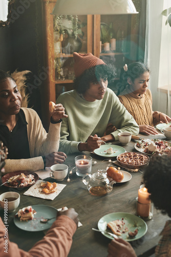 African family sitting at dining table eating homemade pie and drinking tea during family event