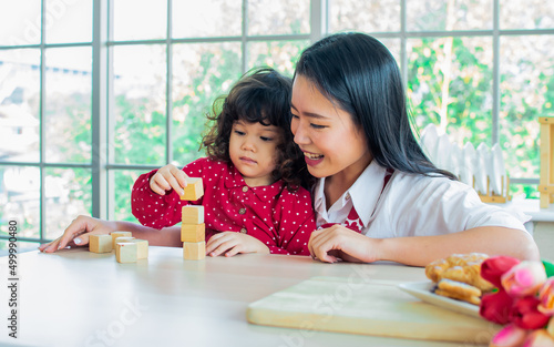 Beautiful Asian woman wearing apron and little cute daughter girl, smiling with happiness, playing together in kitchen at home on Valentine day in morning. Lifestyle, family concept