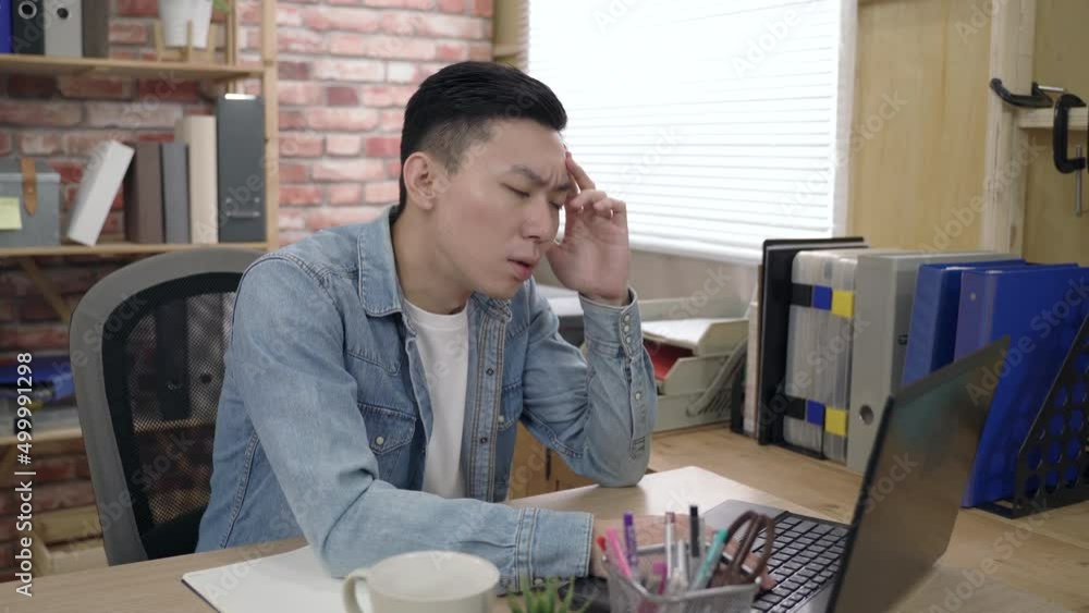 asian young male is propping his head and staring at the monitor while pondering on a difficult project on the computer in the office. asian young male is propping his head and staring at the monitor while pondering on a difficult project on the computer in the office.