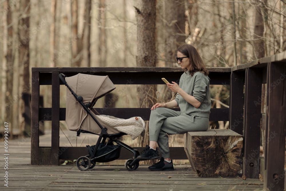 The mom is working with a cellphone while her child is sleeping in the stroller