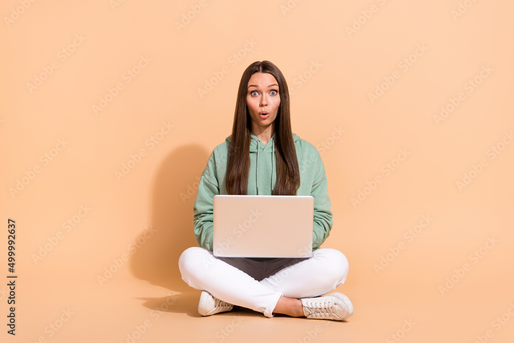 Naklejka premium Portrait of beautiful trendy amazed girl sitting using laptop pout lips isolated over beige pastel color background
