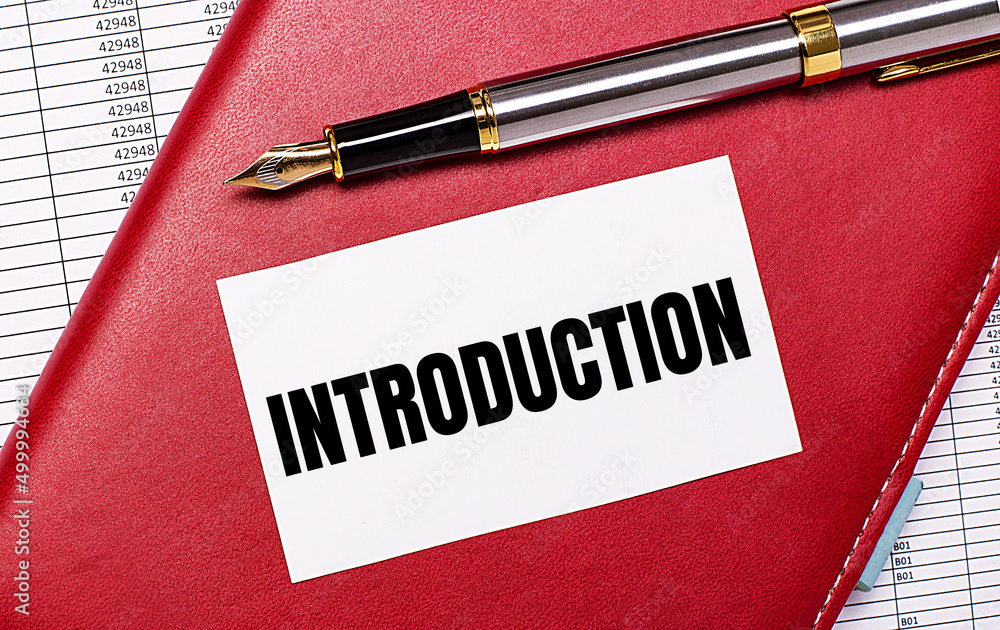 On the desktop there are reports, a burgundy notebook, a fountain pen and a white blank card with the text INTRODUCTION. Business concept On the desktop there are reports, a burgundy notebook, a fountain pen and a white blank card with the text INTRODUCTION. Business concept