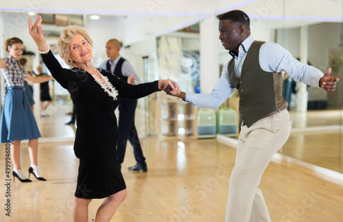 Leinwand Poster Elderly woman learning ballroom dancing in pair in dance studio