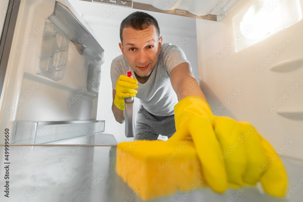 Man in rubber gloves cleans the refrigerator with a sponge and cleaning agent. Photo from inside the refrigerator Man in rubber gloves cleans the refrigerator with a sponge and cleaning agent. Photo from inside the refrigerator