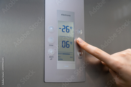 Close-up of a woman's hand regulates the temperature of the refrigerator freezer. Stylish modern grey refrigerator. Woman's hand lowers the temperature to minus twenty-sixteen degrees