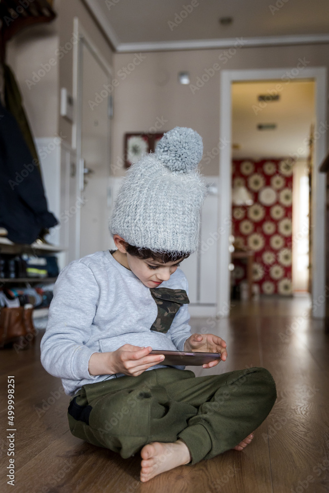 Boy with autism wearing a hat, sitting on the floor while playing with the mobile phone