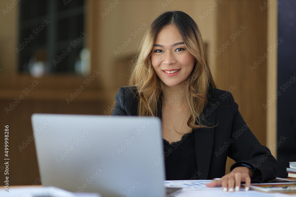 Portrait of a business woman working or secretary with laptop and financial documents on the desk in the office. Looking at camera. Portrait of a business woman working or secretary with laptop and financial documents on the desk in the office. Looking at camera.