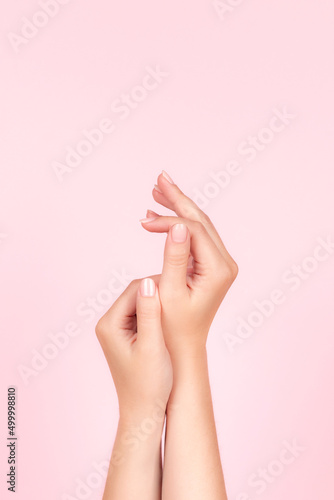 Female hands with beautiful natural manicure - pink nude nails on pink background. Nail care concept