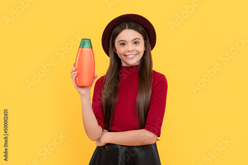glad kid in hat hold hair conditioner bottle on yellow background, hair condition © Olena