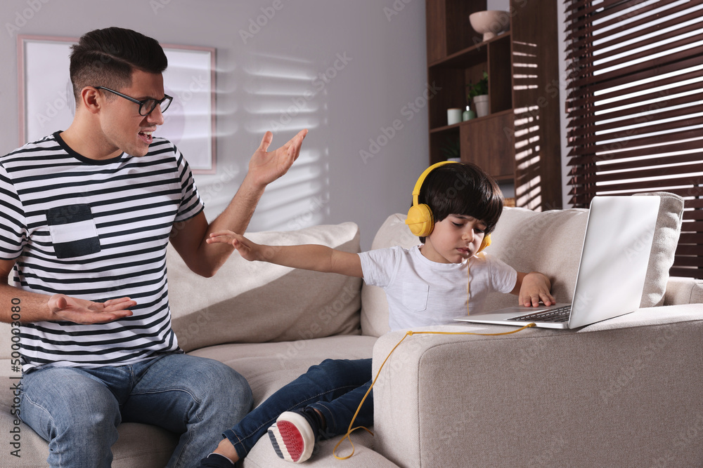 Internet addiction. Man scolding his son while he using laptop in living room Internet addiction. Man scolding his son while he using laptop in living room