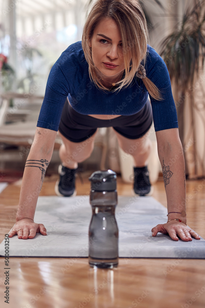 Naklejka premium Pretty woman working out at home. Adult lady with beautiful shaped body exercising in the apartment.