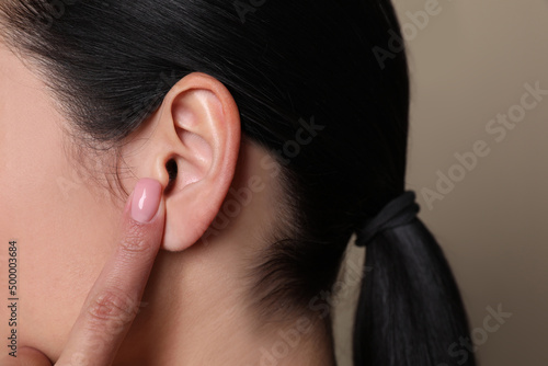 Woman pointing at her ear on grey background, closeup photo