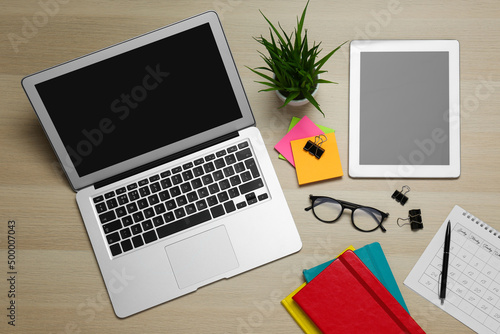 Modern gadgets, glasses and office stationery on wooden table, flat lay. Distance learning