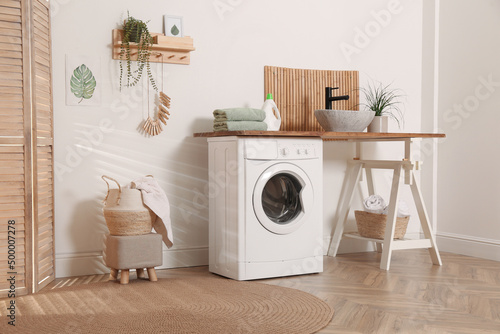 Laundry room interior with modern washing machine and stylish vessel sink on wooden countertop © New Africa