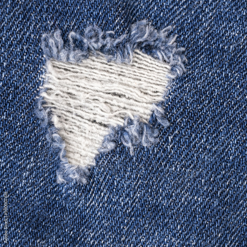 Torn blue jeans with hole material texture, close-up