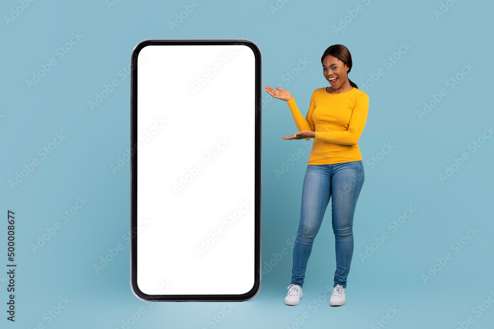 Smiling pretty young african american female with open mouth pointing with hands at huge smartphone Smiling pretty young african american female with open mouth pointing with hands at huge smartphone