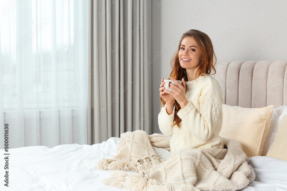Happy beautiful woman with warm plaid and cup of drink in bed at home Happy beautiful woman with warm plaid and cup of drink in bed at home