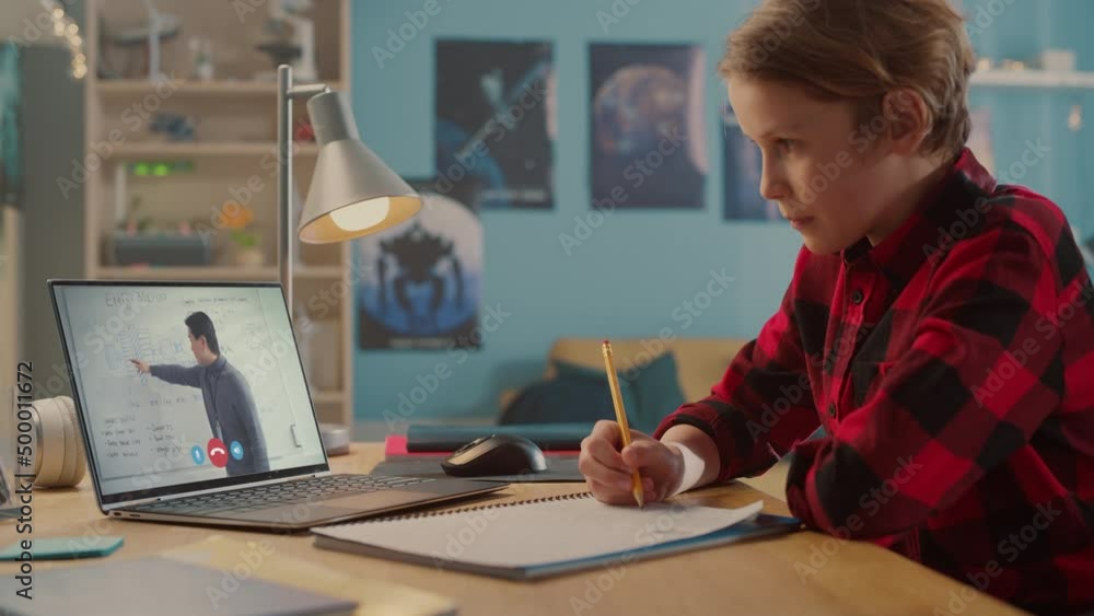 Smart Little Boy Uses Laptop for Video Call with His Teacher. Screen Shows Online Lecture with Teacher Explaining Subject from Classroom, Boy writes Down Information Smart Little Boy Uses Laptop for Video Call with His Teacher. Screen Shows Online Lecture with Teacher Explaining Subject from Classroom, Boy writes Down Information