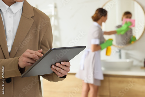 Housekeeping manager with tablet checking maid's work in hotel bathroom, closeup photo