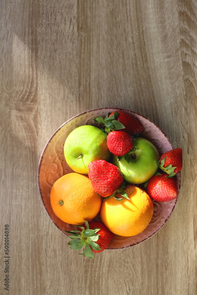 Pink bowl filled with fresh apples, oranges and strawberries on wooden table. Flat lay. Pink bowl filled with fresh apples, oranges and strawberries on wooden table. Flat lay.