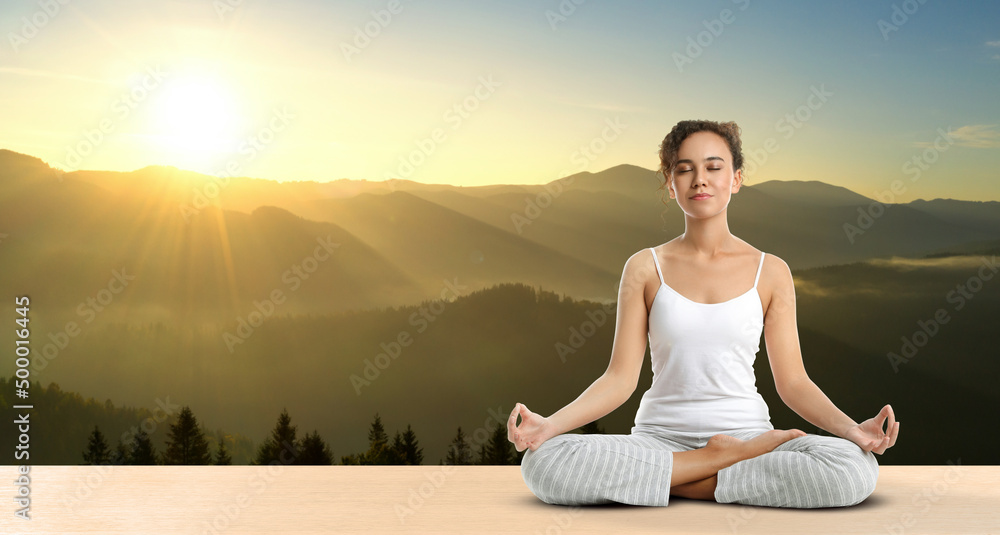 Young African American woman practicing yoga on wooden surface against beautiful mountain landscape, space for text. Banner design