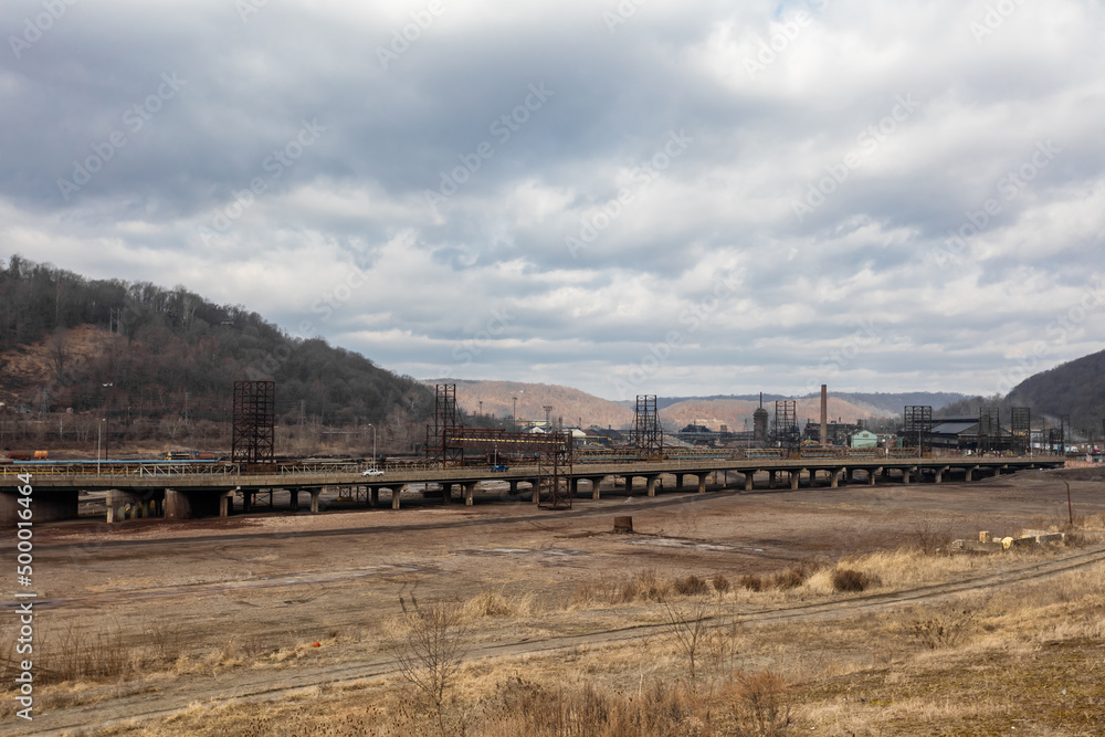 Wide open industrial field in front of a bridge crossing an abandoned steel mill in a small midwest town Wide open industrial field in front of a bridge crossing an abandoned steel mill in a small midwest town