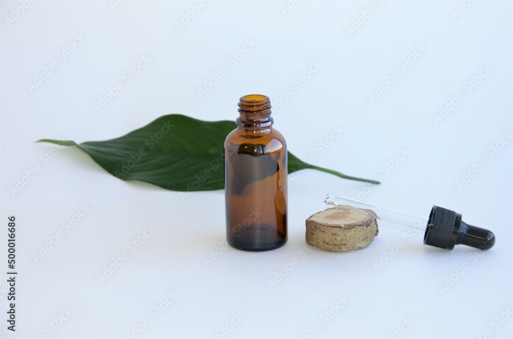 cosmetic glass bottle with a sheet of greenery on a white background