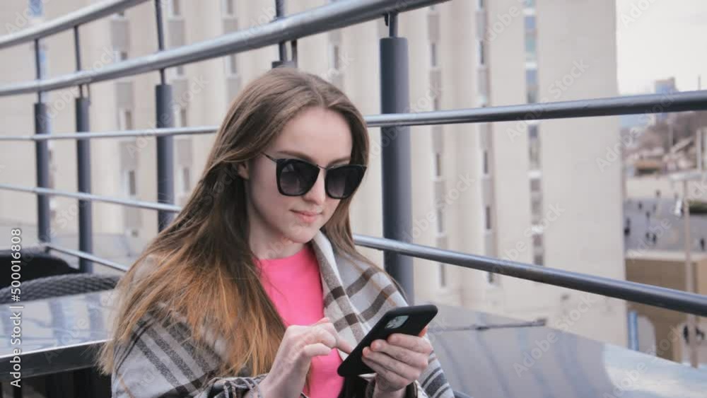A beautiful young girl sits in a summer cafe and writes a message on her smartphone outside A beautiful young girl sits in a summer cafe and writes a message on her smartphone outside