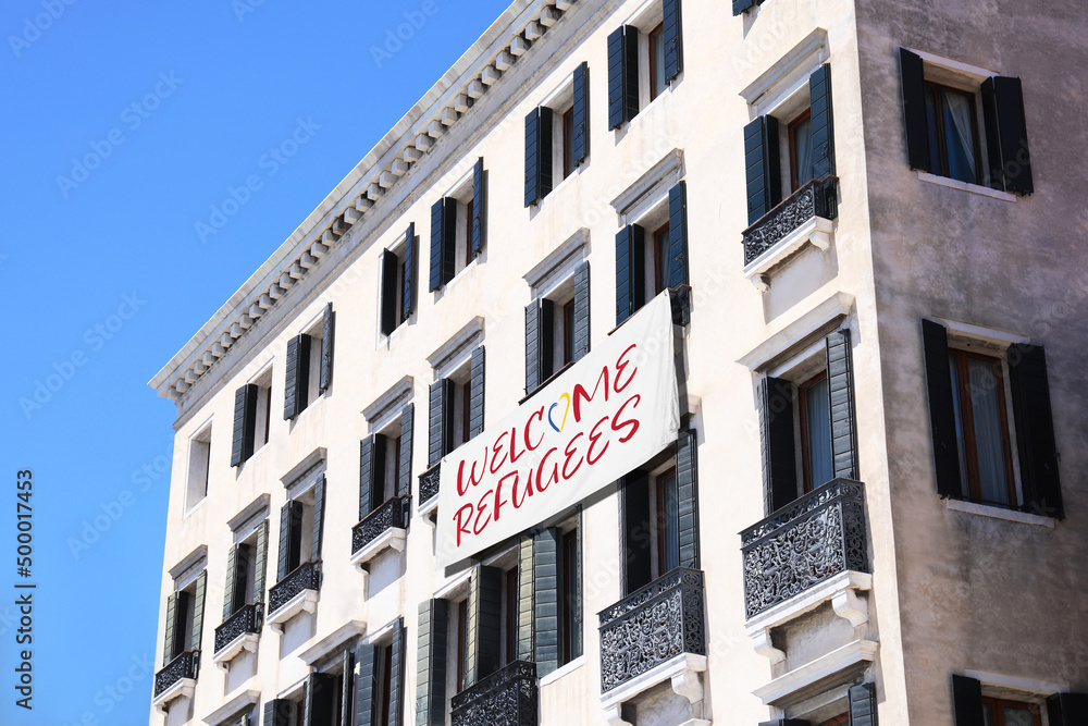 Banner with phrase WELCOME REFUGEES on building outdoors Banner with phrase WELCOME REFUGEES on building outdoors