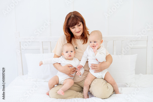 happy grandmother with two grandchildren baby at home on the bed hugs and kisses